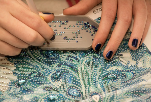 Mains réalisant un diamond painting aux teintes bleues