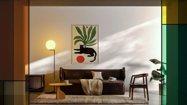 Salon moderne avec une affiche de plante et de chat noir au-dessus d’un canapé en cuir, à côté d’une lampe boule allumée