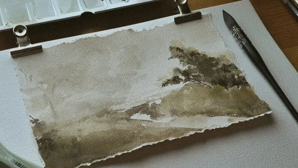 Aquarelle de paysage sur papier à grain, palette et pinceau sur une table d’atelier